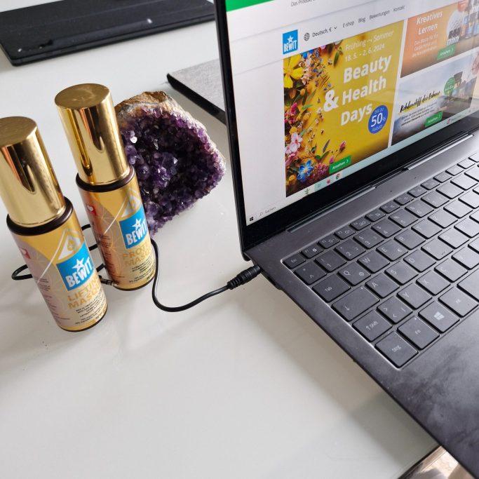 Zwei Flaschen mit Goldkappen stehen neben einem Laptop auf einem Tisch.