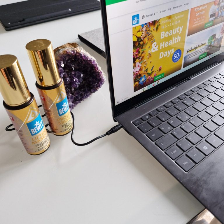 Zwei Flaschen mit goldenen Deckeln stehen neben einem Laptop auf einem Tisch.